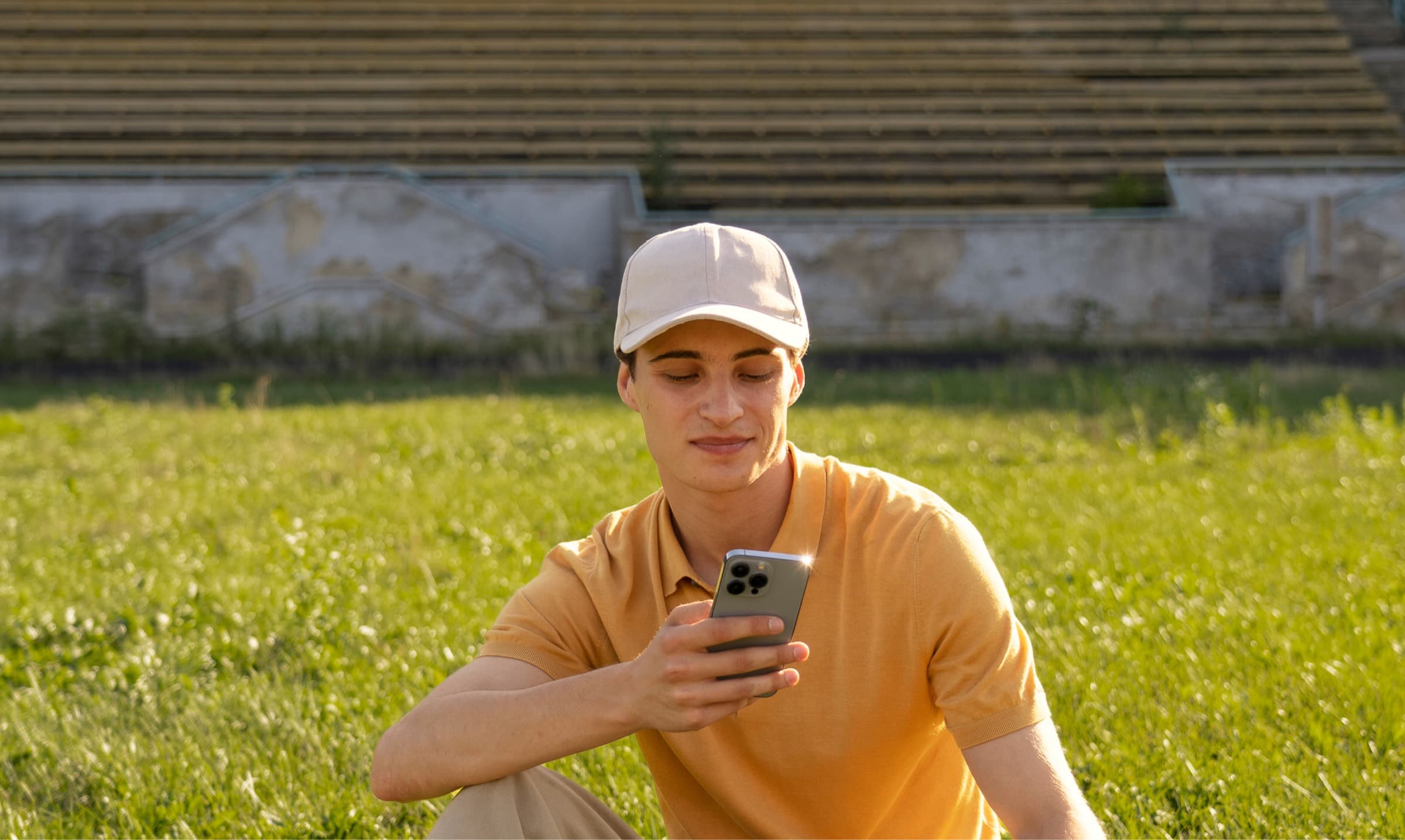 A man sitting on a lawn, smiling at his phone