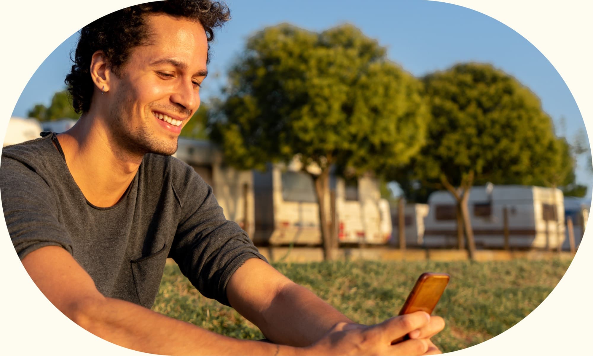 A man lying on grass in a park at sunset, using his phone